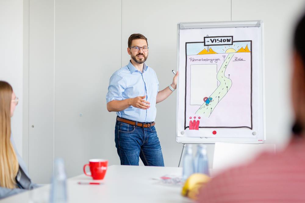Young man standing in front of a flip chart, welcoming his audience to a coaching workshop